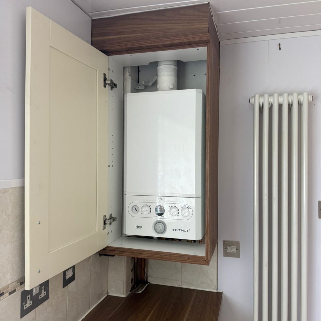 Boiler fitted in a hallway cupboard beside a column radiator