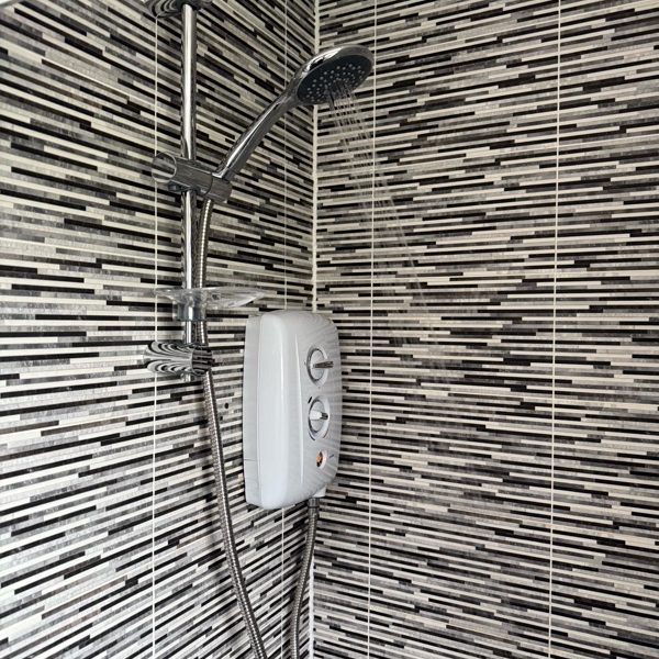 Electric shower installed over a mosaic-tiled wall